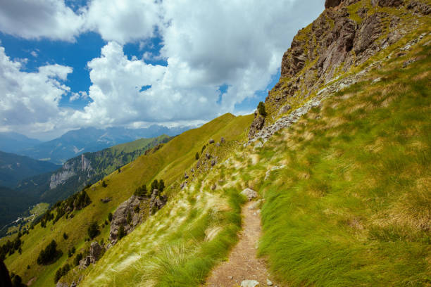 Summer time in Dolomites. landscape with hills, clouds, grass and trail.