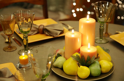 Elegant table or place setting with eco-friendly decorations, including fruit and burning candles. Horizontal image.
