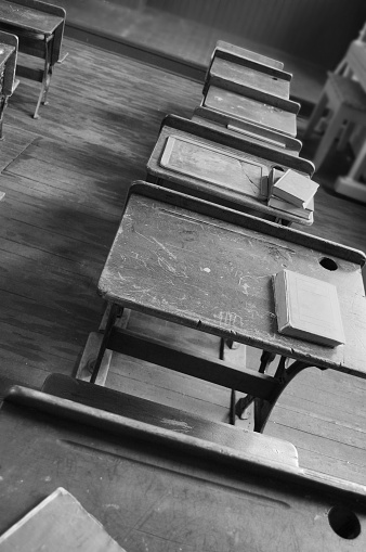 A row of old wood student desks in a classroom in black and white.
