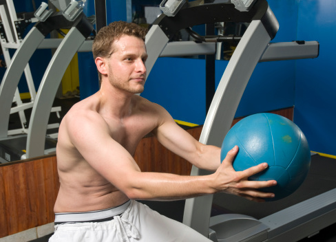Man posing in front of a treadmill with a medicine ball