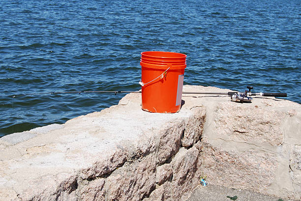 A fishing rod and bucket on a stone fishing pier.
