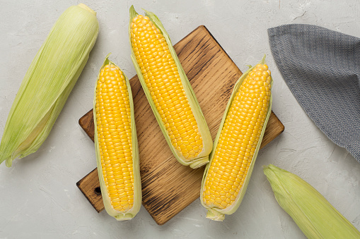 Fresh corn on cobs on concrete background, top view