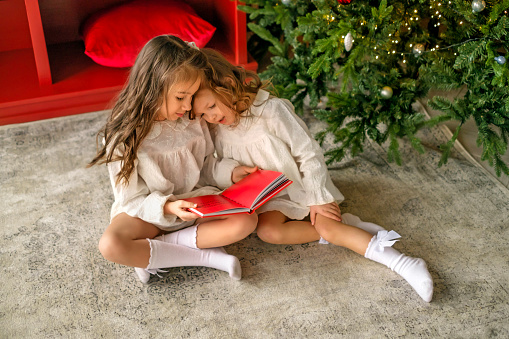 Children are reading a book with Christmas fairy tales. The girl put her head on her sister's shoulder, dreaming and listening to the story