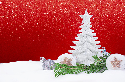 White shiny Christmas tree with silver balls and stars with pine branch on snow on side, behind sparkle red background. New Year. Copy space