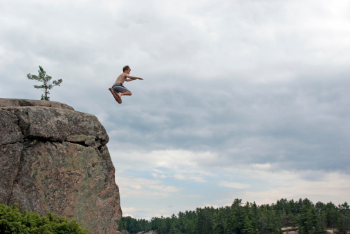 A teenaged boy show off his courage by jumping off a cliff into a deep boy of water while on vacation.