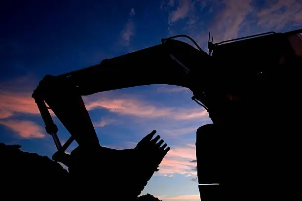 A silhouette large earth moving machine shot using a wide angle lens.  The hydraulic excavator was shot against a blue sky with scattered clouds during sunset.