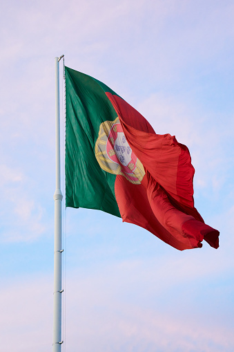 National flag of Portugal flutters in the wind against the blue sky. Democracy and politics. European country. Vertical
