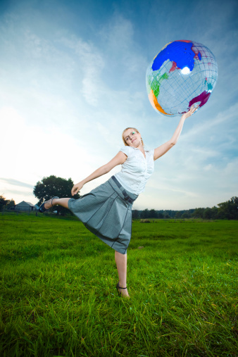 Young smiling lady posing with an inflatable globe with her leg and arm up.