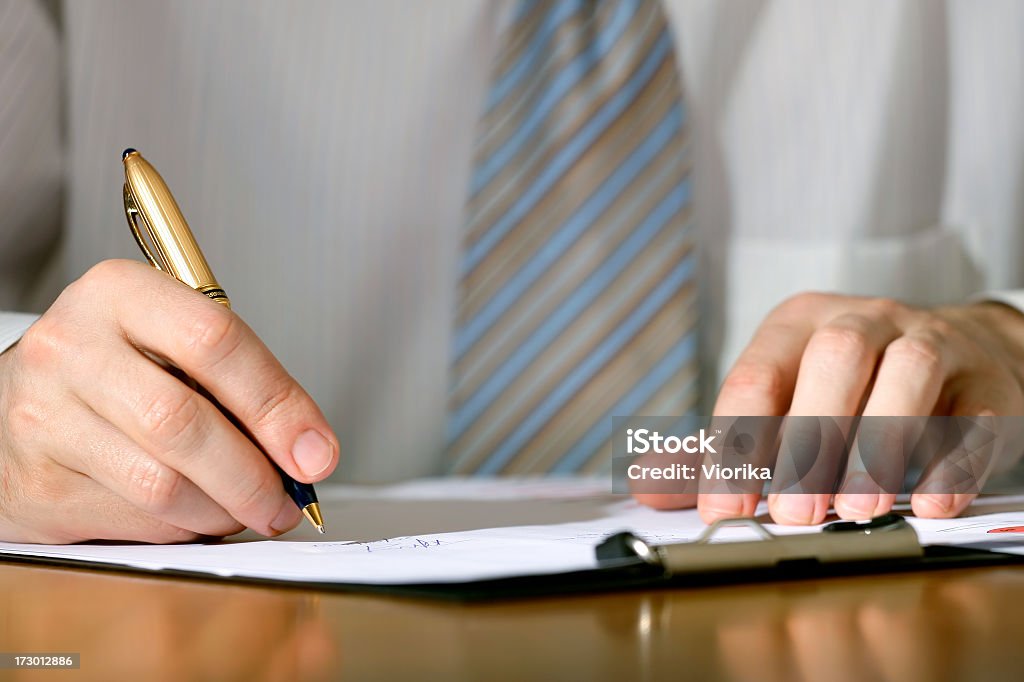 Signing document on a clipboard Close-up of a businessman's hand with a gilded pen writing something. Shallow depth of field. Clipboard Stock Photo