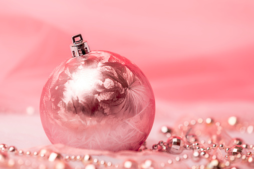 A pink Christmas ornament with a tree and accents on a pink background with room for copy.