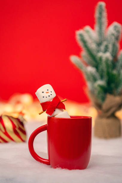 A marshmallow snowman in a red scarf smiling as he relaxes in a mug of hot chocolate.