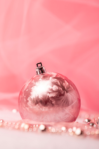 A pink Christmas ornament with a tree and acecents on a pink background with room for copy.