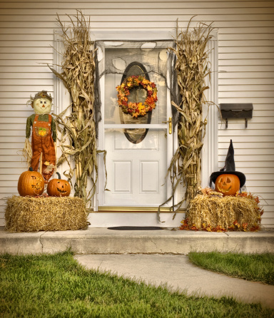 A scarecrow, hay, pumpkins, corn stalks, and an autumn wreath create a warm and cozy front door scene. High Dynamic Image
