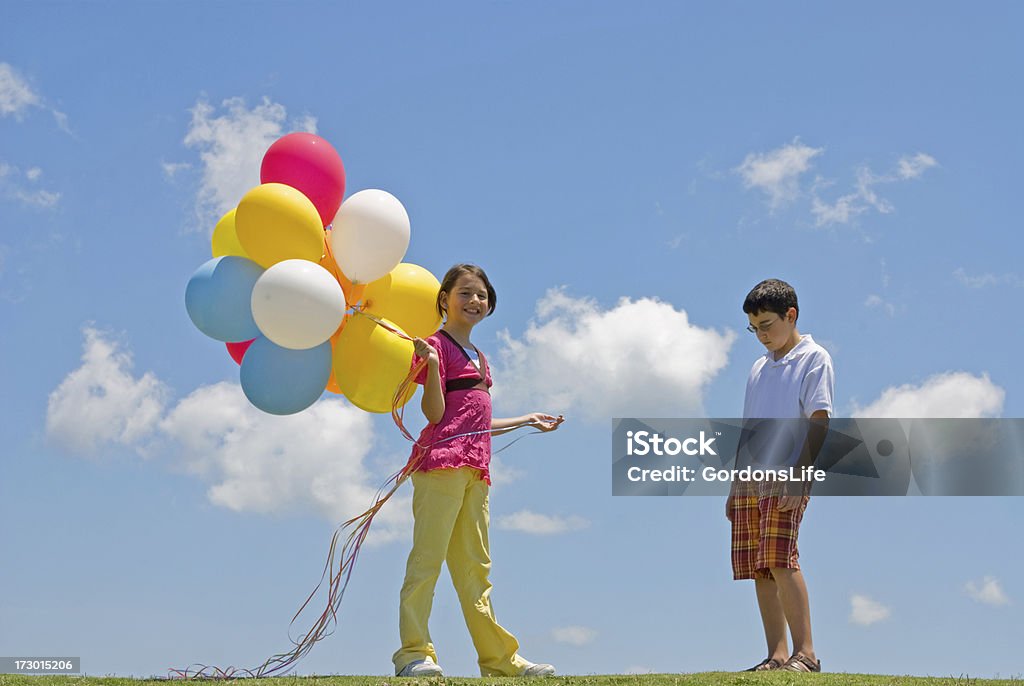 Girl with Balloons Happy - Boy without Sad A hispanic boy and a girl on a hill with bright blue sky and colorful balloons.  Girl is smiling holding balloons and boy is sad and without any. Balloon Stock Photo