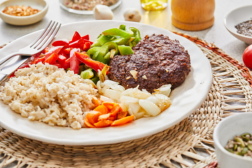 Beef meat, rice and fresh vegetables, a healthy protein lunch after the workout, made of beef meat, green pepper, red pepper, carrot, onion, rice and garlic, served in a modern plate on a grey rustic home or restaurant ceramic marble table, representing a wellbeing and a healthy lifestyle, an image with a copy space