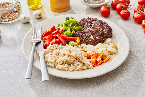 Beef meat, rice and fresh vegetables, a healthy protein lunch after the workout, made of beef meat, green pepper, red pepper, carrot, onion, rice and garlic, served in a modern plate on a grey rustic home or restaurant ceramic marble table, representing a wellbeing and a healthy lifestyle, an image with a copy space