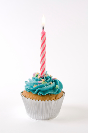 A pink birthday candle lit on a cupcake with blue icing and multi-colored stars.