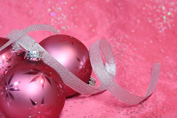 Three Glittery pink ornaments and silver ribbon on sparkling pink background with copy space. Horizontal Christmas image.