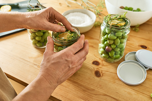 Woman preparing fermented olives in glass jar with slices of lemon, wild fennel and canning brine. Autumn vegetables canning. Healthy homemade food. Conservation of harvest.