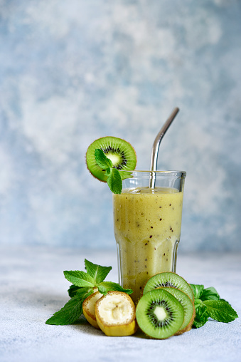 Kiwi and banana smoothie with mint in a tall glass on light blue slate, stone or concrete background.