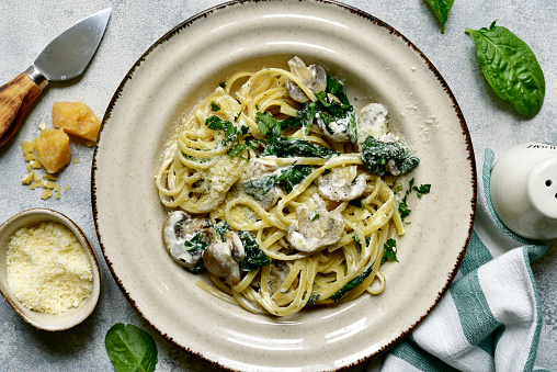 Pasta with spinach and mushrooms in a cream sauce on a light grey slate, stone or concrete background. Top view with copy space.