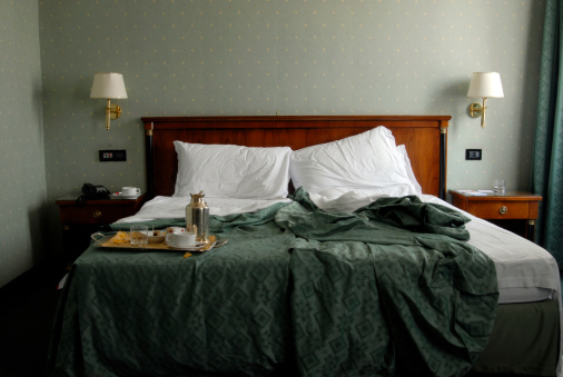 Unmade hotel bed with breakfast tray