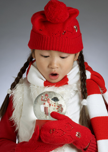 Young Asian girl holding Snow Globe and surprised to see herself inside the tiny winter wonderland.