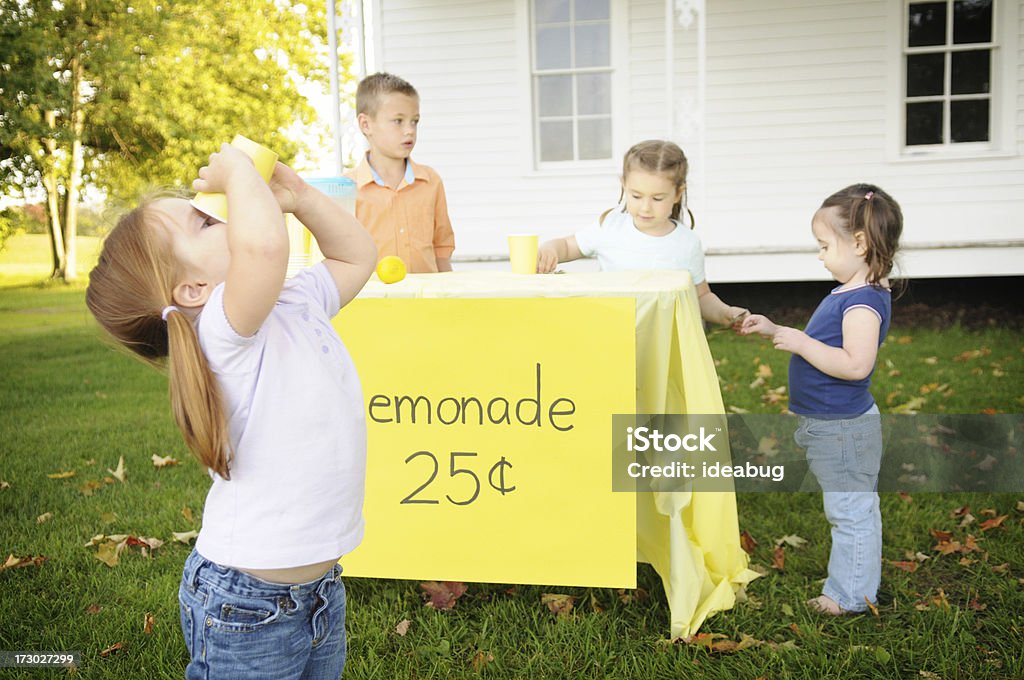 Mała dziewczynka pije Lemoniada z przodu stanowiska - Zbiór zdjęć royalty-free (Stoisko z lemoniadą)