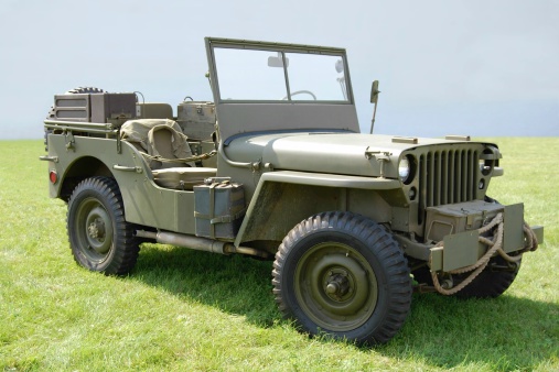 Classic WWII army jeep on grassy field in front of hazy gray background.