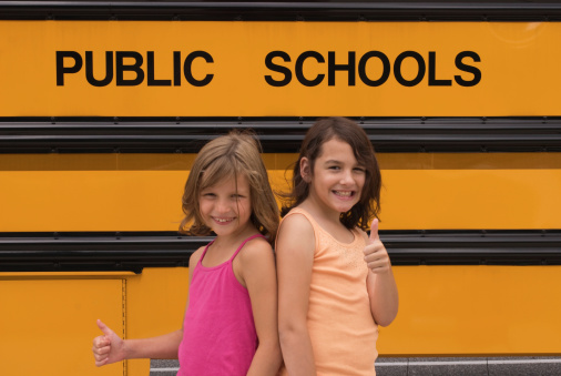 Two little girls with thumbs up for public school ... orange of a school bus with public school lettering  in the background.                                                                                                                                                                                                                                                                                                                              My entire school bus series can be found here:  http://www.istockphoto.com/file_search.phpaction=file&lightboxID=2781718
