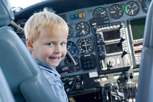 Child looking back over his shoulder at the camera, whilst sat in a leather seat of a cockpit in a private plane. See more in this series.