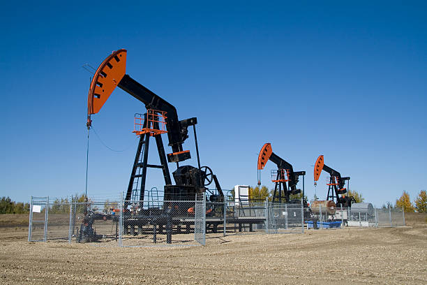 Pumpjack Herd Three orange and black pumpjacks in a row on a clear blue day. wellhead stock pictures, royalty-free photos & images