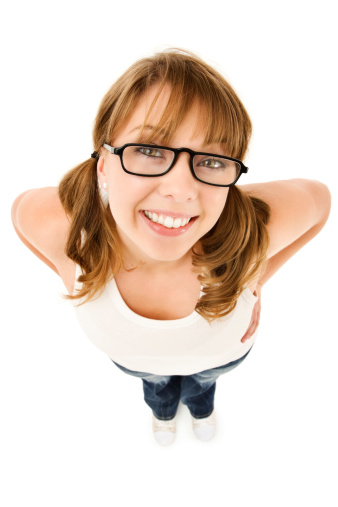 Closeup high-angle wide shot of a teenage girl nerd wearing black rimmed glasses and a bright happy smile.