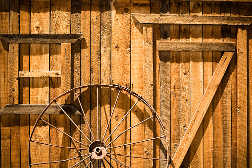 An abandoned wagon wheel leans against a barn in Utah