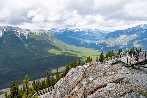 Banff, AB, Canada-July 7, 2023; High level panoramic view from top of Sulphur Mountain with people on boardwalk and Bow River and surrounding mountains in background