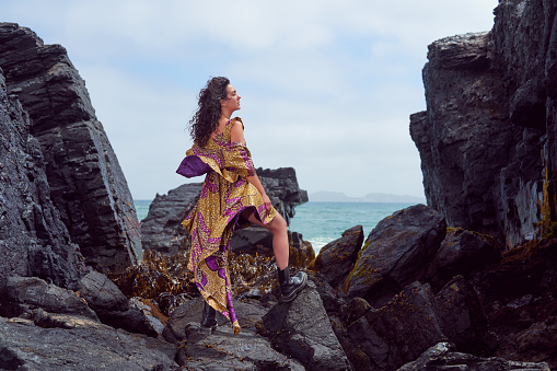 portrait beauty fashion full body woman with dress and boots posing on the rocks with ocean in the background