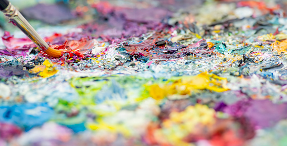 A wet brush dips into an oil paint palette, revealing vibrant colors, capturing artistic creation's essence.