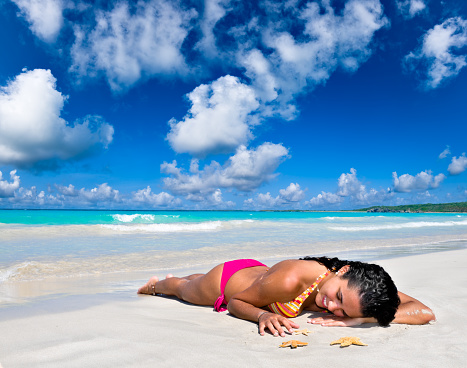 Young woman lying relaxed on a Tropical white sand beach. Relaxing images of travel and leisure related vacation themes for vacations in the Caribbean. Image taken at Los Roques, Venezuela. Los Roques is an archipelago or group of small islands located at 80 miles north of the Venezuelan coastline and a very popular destination for leisure, diving, kite surfing and all king of water activities. Los Roques and the beauty of the turquoise coastal beaches of Venezuela are almost indistinguishable from those of the Bahamas, French Polynesia, Malau, Hawaii, Cancun, Costa Rica, Florida, Maldives, Cuba, Fiji, Bora Bora,  Puerto Rico, Honduras, or other tropical vacation travel destinations.