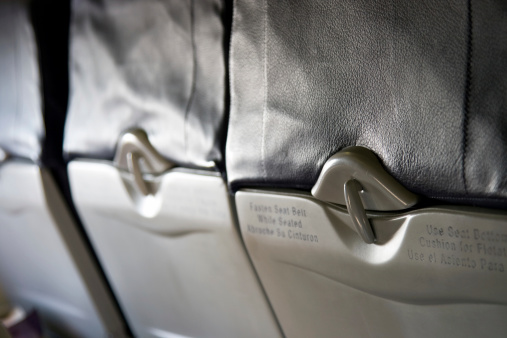 A row of upright lap trays on the backs of seats on an airplane. Shallow depth of field. Focus on nearest clasp.