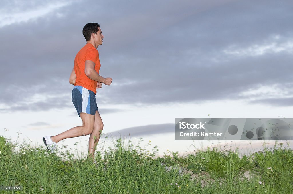 running Maschio adulto con un top arancione e pantaloncini blu - Foto stock royalty-free di Abbigliamento sportivo