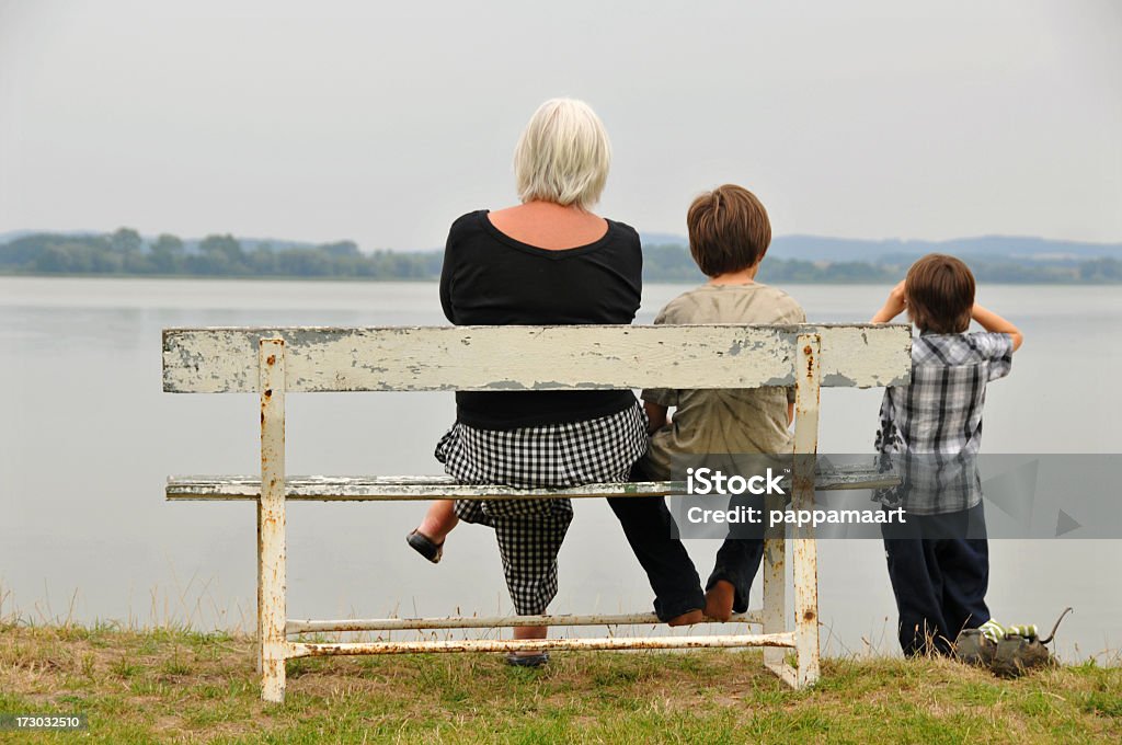 Mamie avec grandsons sur un banc au bord de l'eau - Photo de Regarder libre de droits