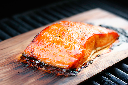 Salmon fillet with coarse ground pepper, grilled over a cedar plank.  This cooking method gives the salmon great cedar smoke flavor and color.  Shallow dof.