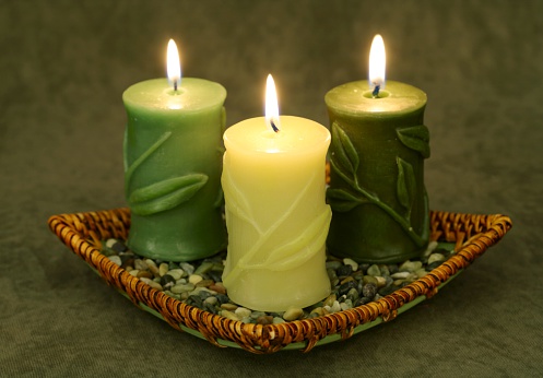Trio of burning candles embossed with bamboo leaves, in basket with pebbles. Horizontal image.