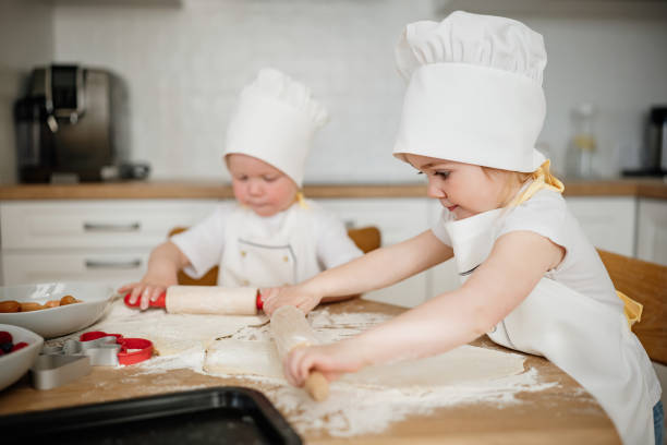 istock Adorable kids in chef hats and aprons rolling out pastry dough 1730343288