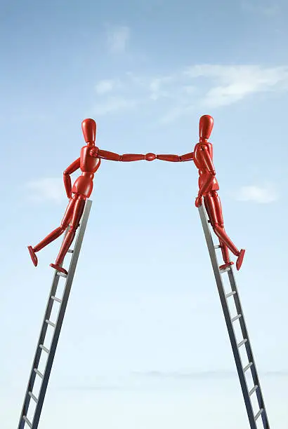 Two figures shake hands while standing on ladders.