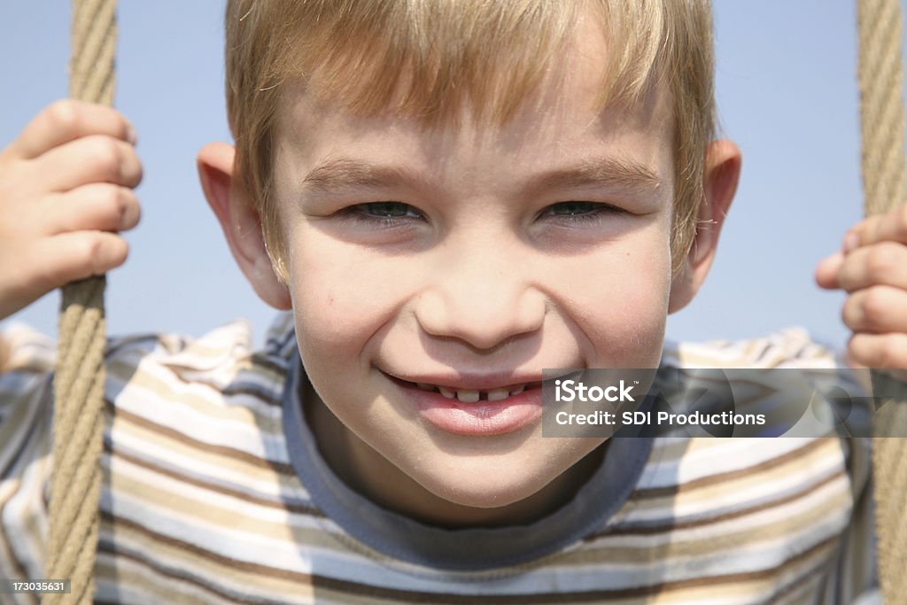 Happy Smiling Boy Hanging On Ropes A happy young boy holding on to playground ropes. 4-5 Years Stock Photo