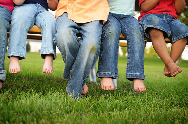 dirty las piernas y cuadrados de niños sentado en un banco de - child human foot barefoot jeans fotografías e imágenes de stock