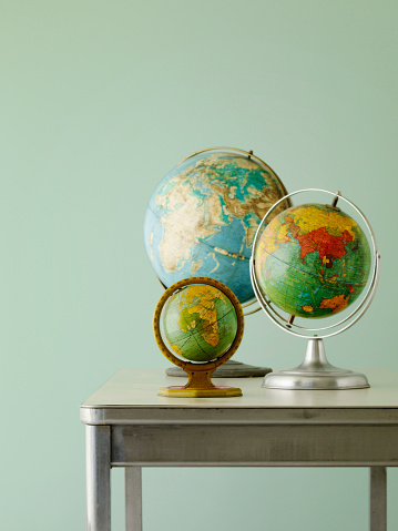Still life image of three vintage globes on a desk photographed against a green toned background with selective focus.