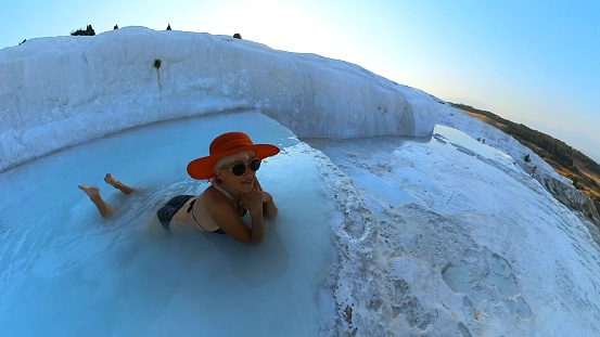 moment of relaxation of tourist woman immerses herself in crystal-clear waters of Turkey Pamukkale's natural pools. Surrounded by surreal white terraces, embraced by soothing warmth of thermal springs