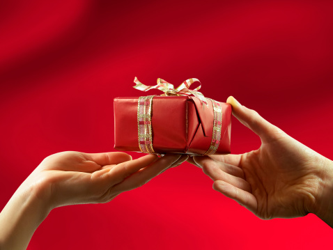 Close-up of red gift box with ribbon, giving from man to woman.